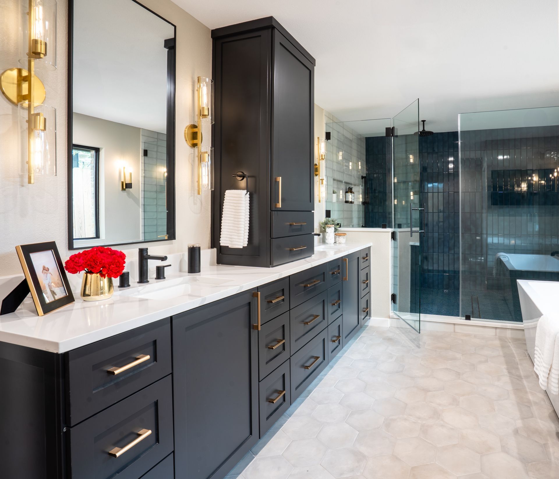 Modern bathroom with dark navy cabinets, white countertop, gold sconces, and glass shower enclosure