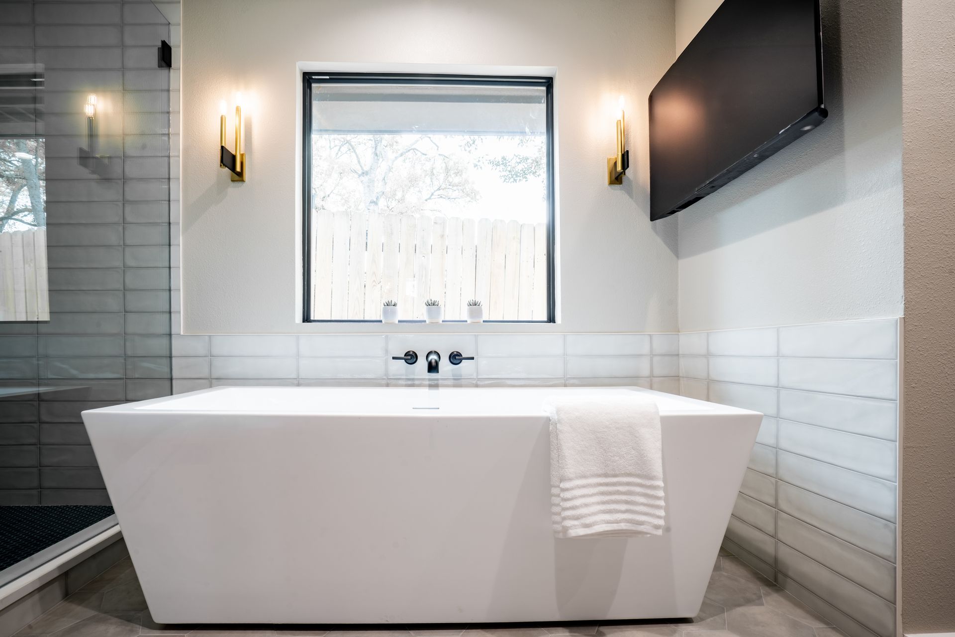 Modern bathroom with freestanding white tub beneath a window and wall sconces