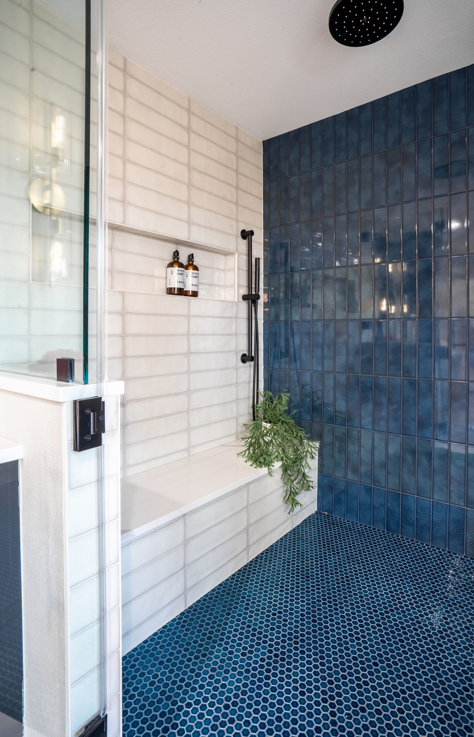 Blue-tiled shower with white bench, glass enclosure, and patterned blue floor in a modern bathroom