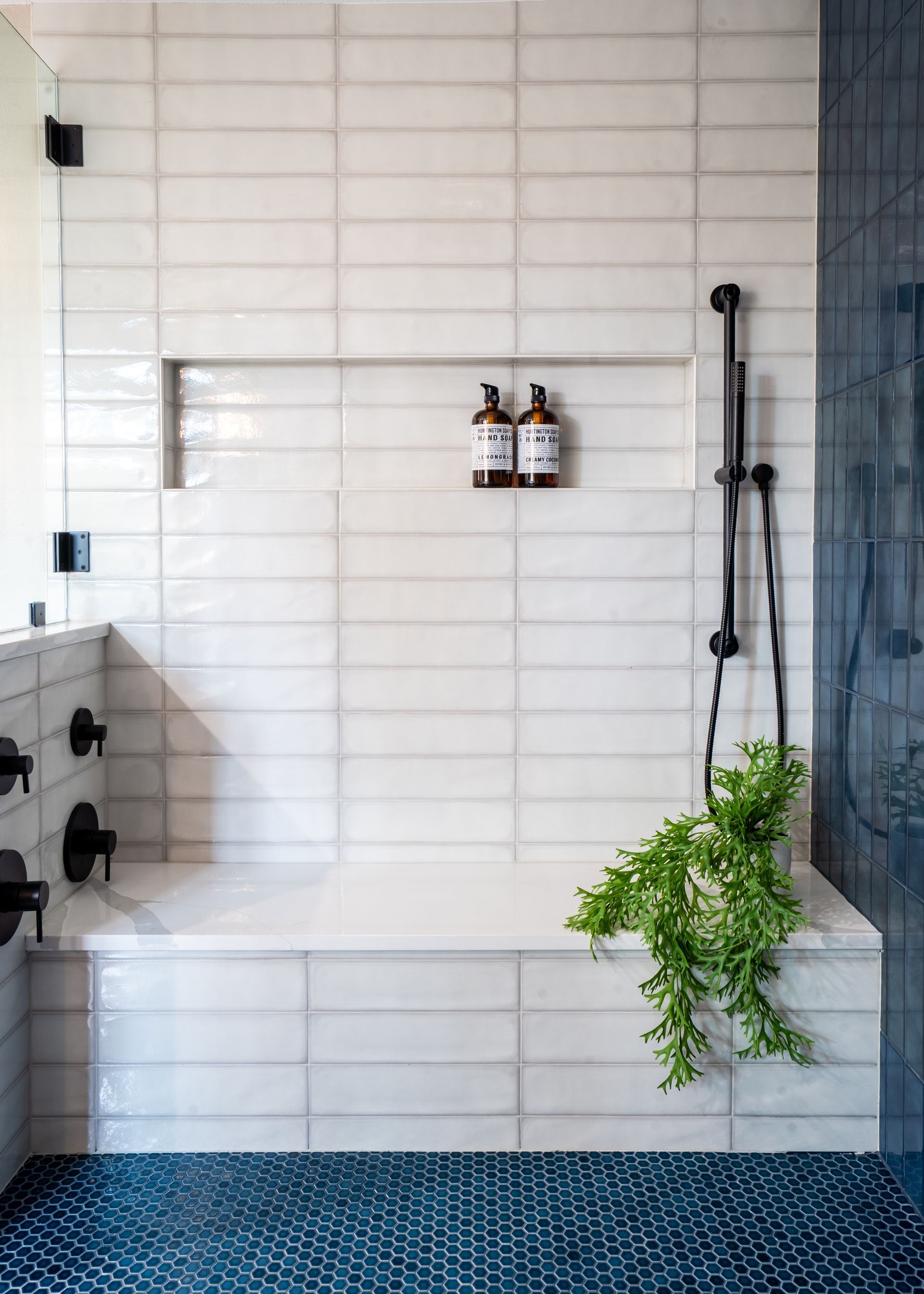 Modern white-tiled shower with black fixtures and hanging green plant on the side.