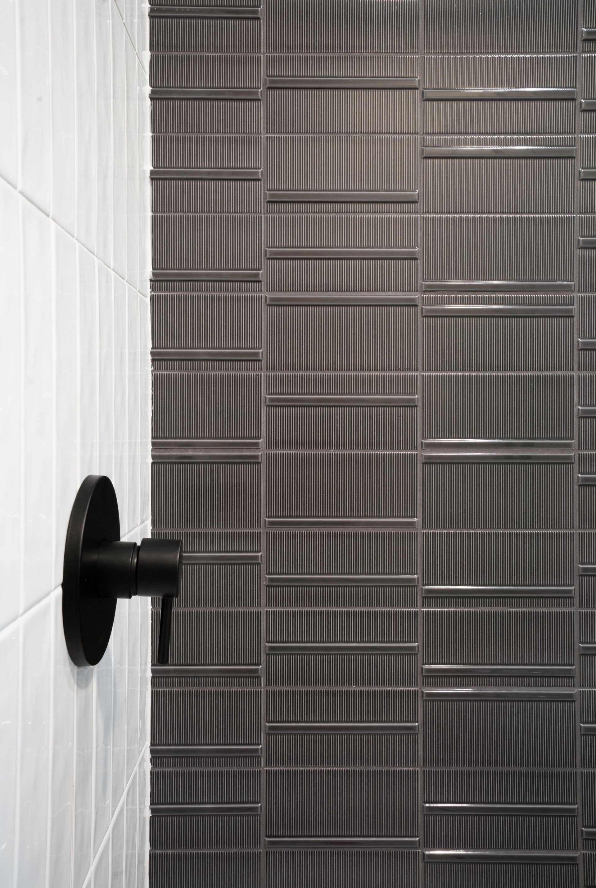 Bathroom corner with white tile, gray patterned shower curtain, and black wall-mounted fixture