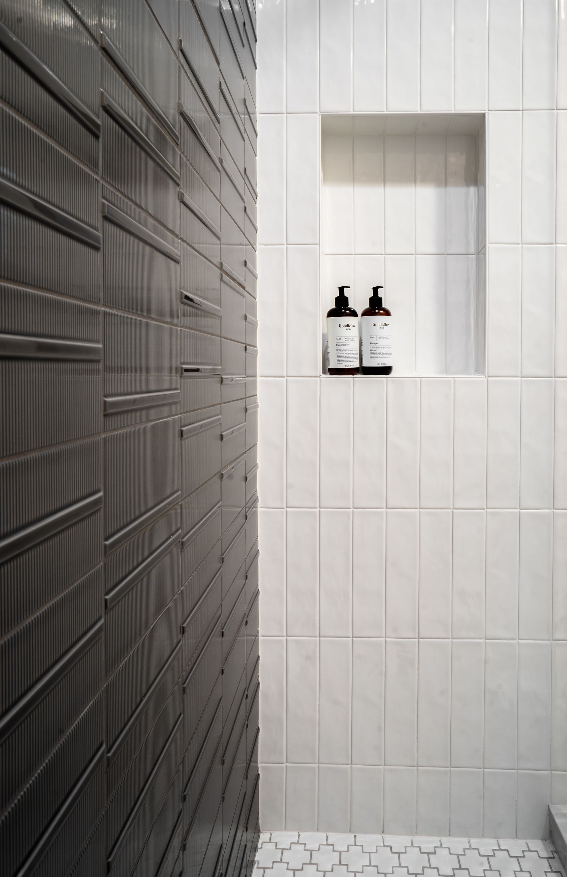Modern shower with gray tile walls and two bottles on a recessed shelf.