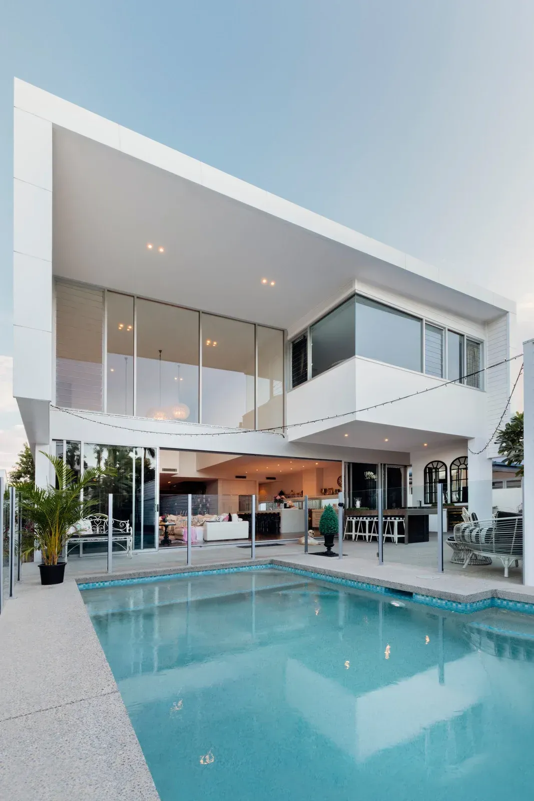 Modern white house with a turquoise pool and open patio at dusk