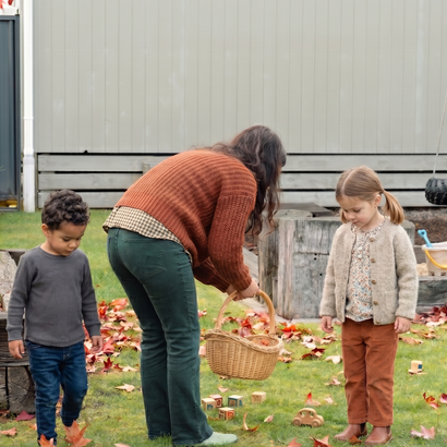 Woman and two children in backyard collecting fallen leaves with a basket.