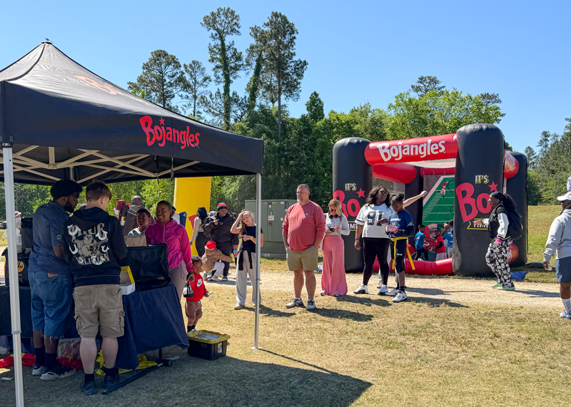 Outdoor community event with Bojangles signs, vendor tents, and people gathered on a sunny lawn