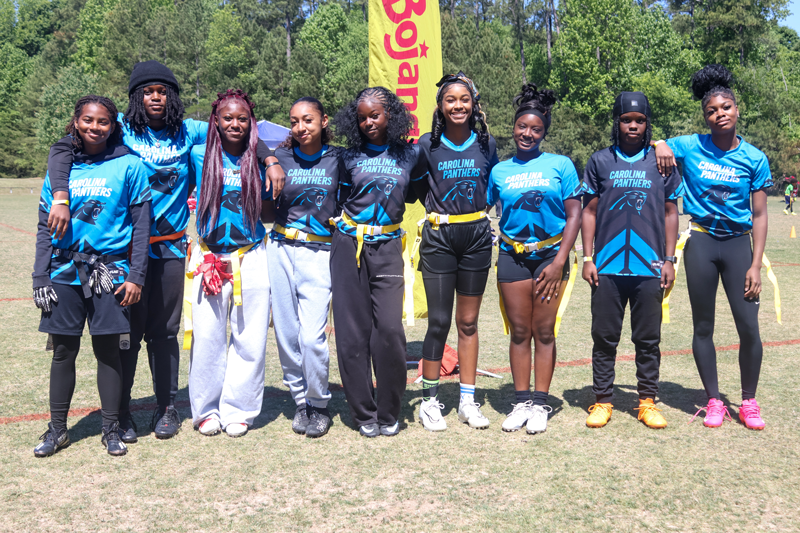 Group of flag football players in blue shirts posing outdoors with a yellow banner behind them