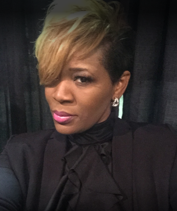 Woman with blonde-tipped hair and pink lipstick wears a black jacket and gazes at the camera.