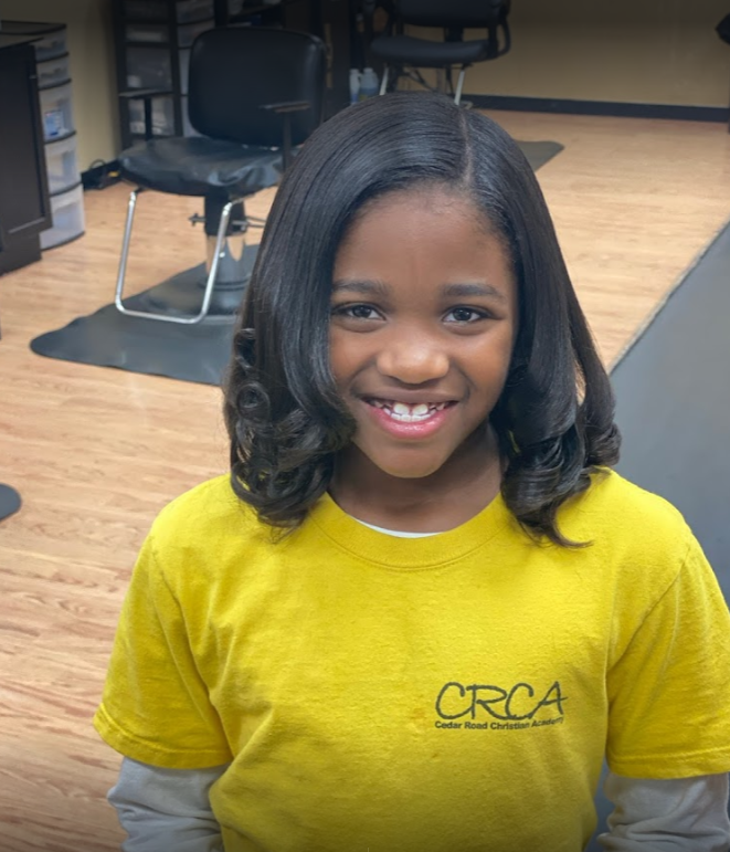 Smiling young girl with straightened black hair, wearing a yellow shirt, in a salon.