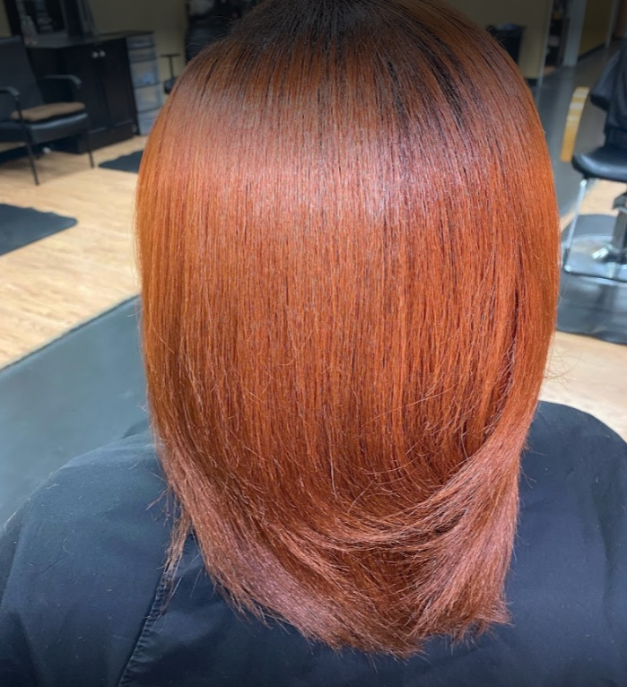 Woman with sleek, auburn-colored, straight hair, styled in a long bob at a salon.