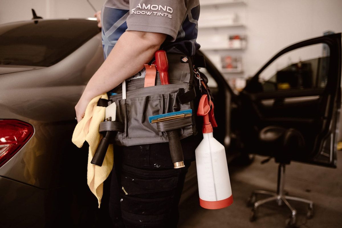 Technician with Tool Belt and Spray Bottle Standing Beside a Car — Diamond Window Tints in Phillip, ACT