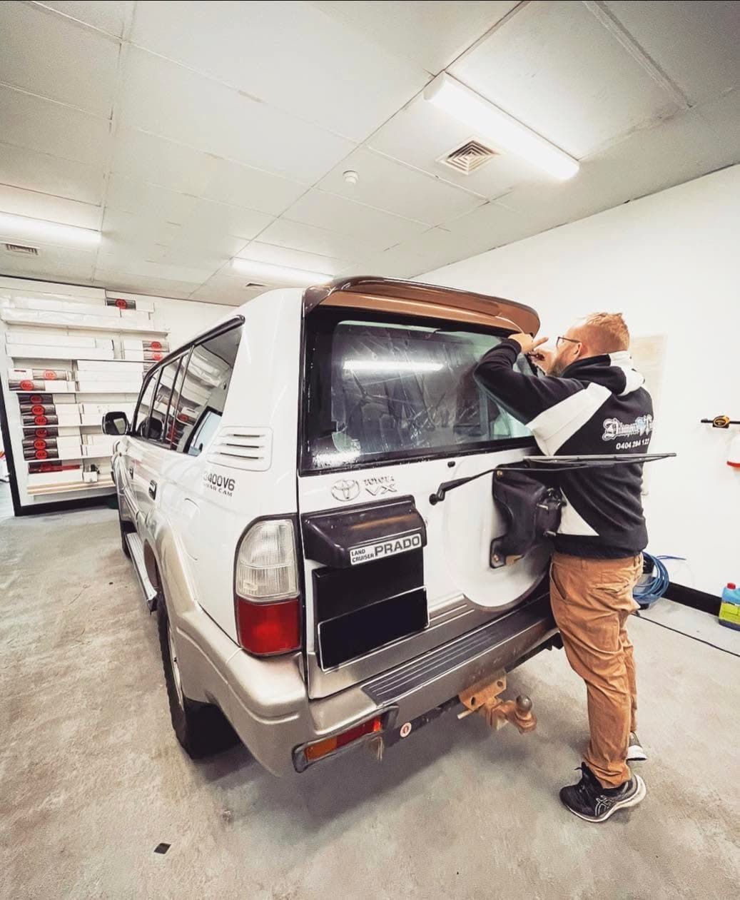 Person Adjusting the Rear Window of A White Suv in A Garage-Like Workshop — Diamond Window Tints in Phillip, ACT