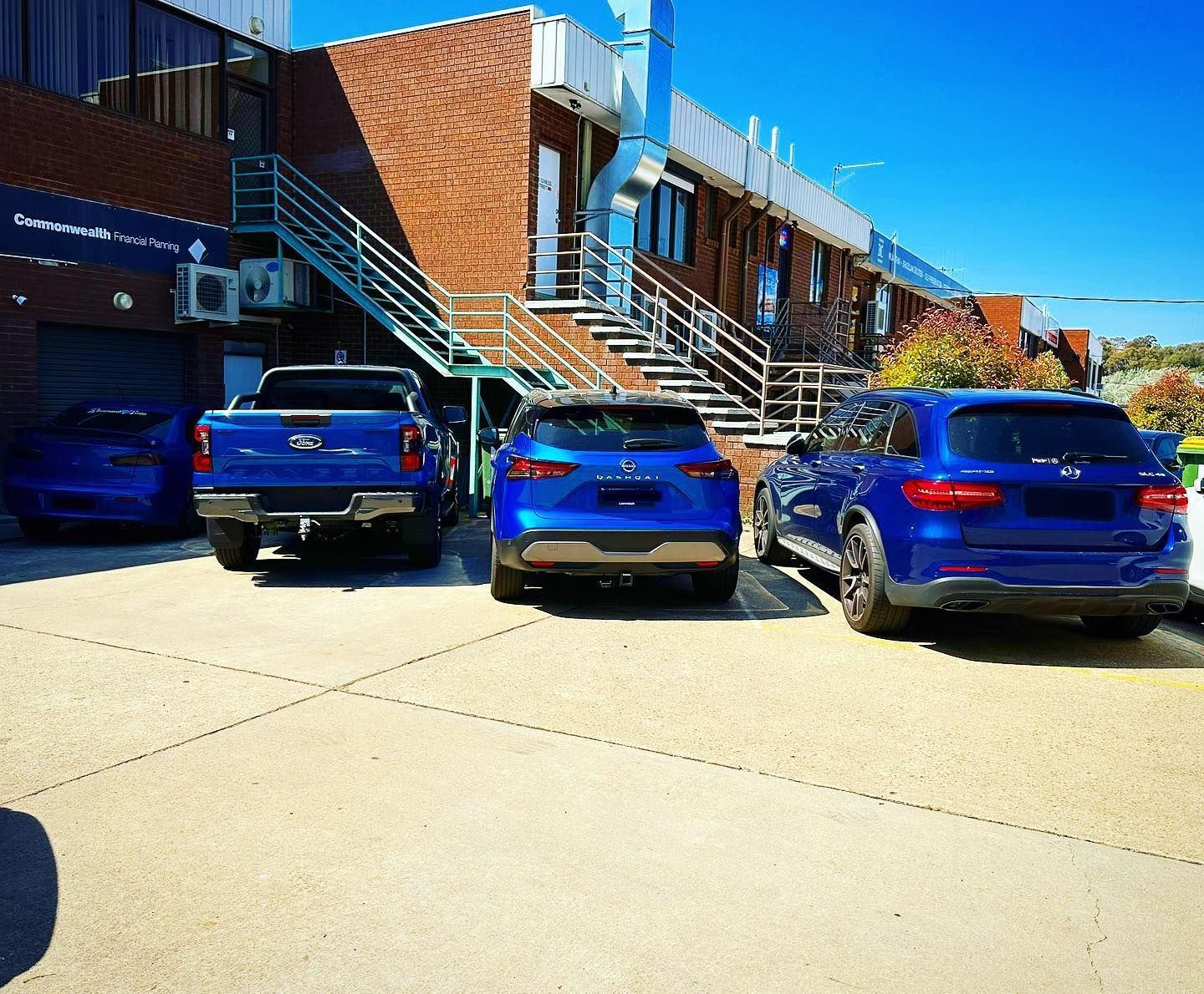 Four blue vehicles parked in front of a brick building with stairs; sunny day. — Diamond Tints In Phillip, ACT
