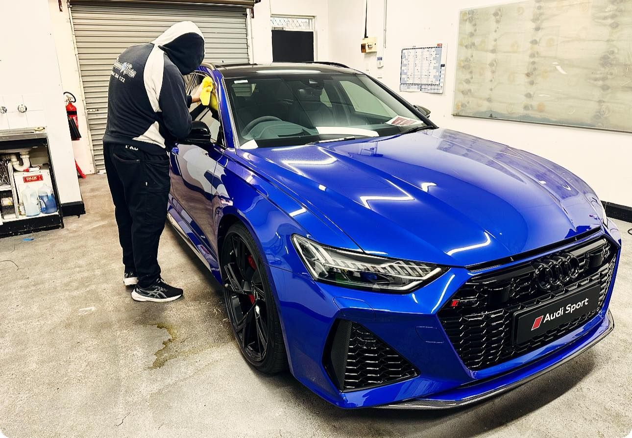 A Man is Polishing a Blue Car in a Garage — Diamond Tints In Phillip, ACT