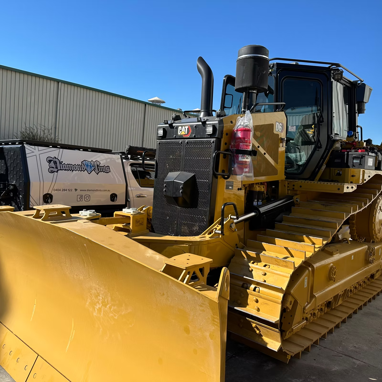 A Yellow Bulldozer is Parked in Front of a Building — Diamond Tints In Phillip, ACT