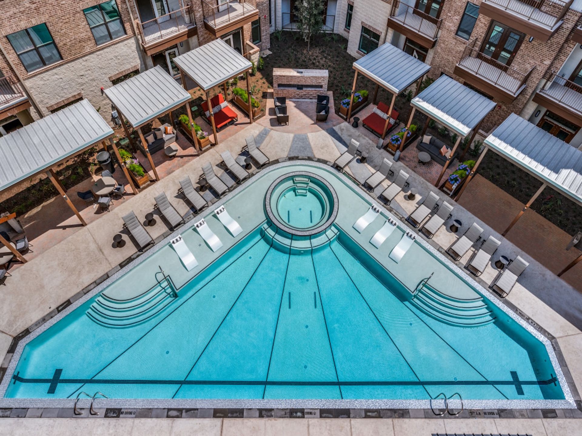 Aerial view of a turquoise courtyard pool with lounge chairs and apartment balconies around it