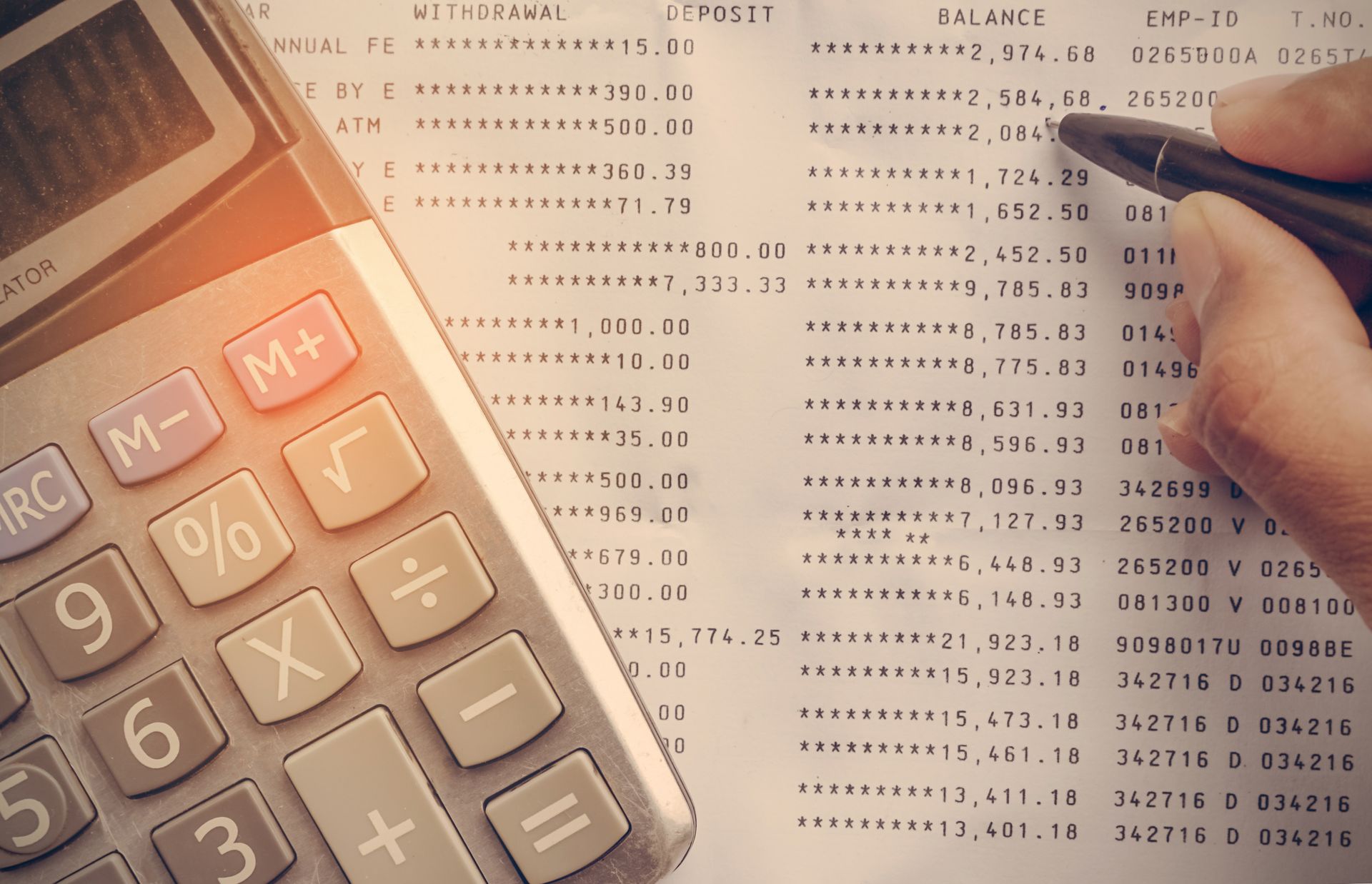 Calculator and a hand holding a pen pointing at a financial ledger with numbers, likely calculating a balance.