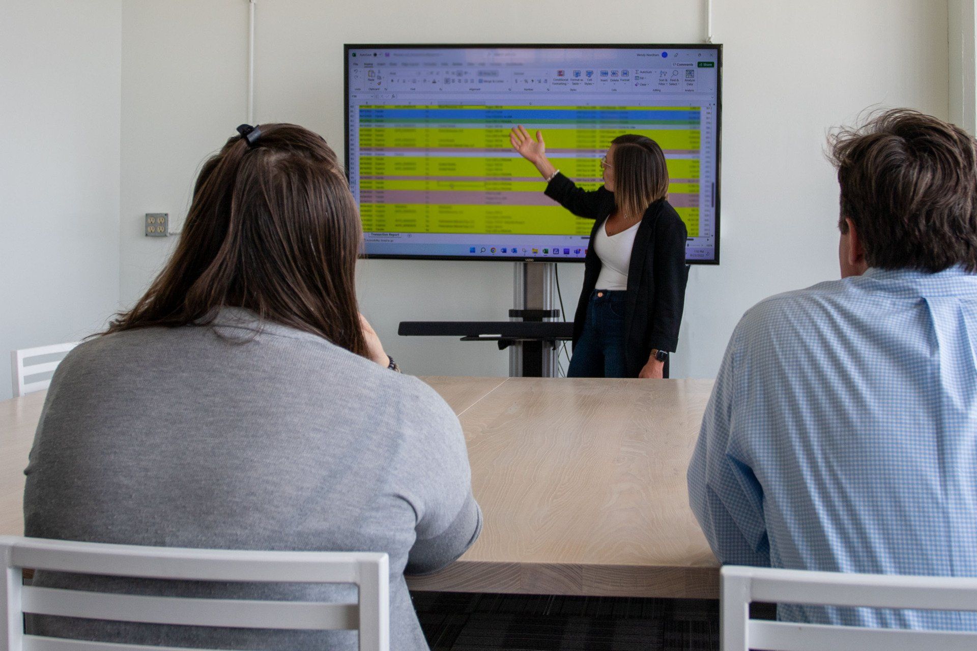 Woman presenting a spreadsheet on a screen to two people in a meeting.