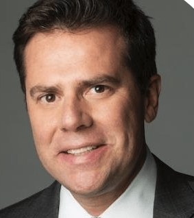 Smiling man in a suit, headshot against a neutral gray background.