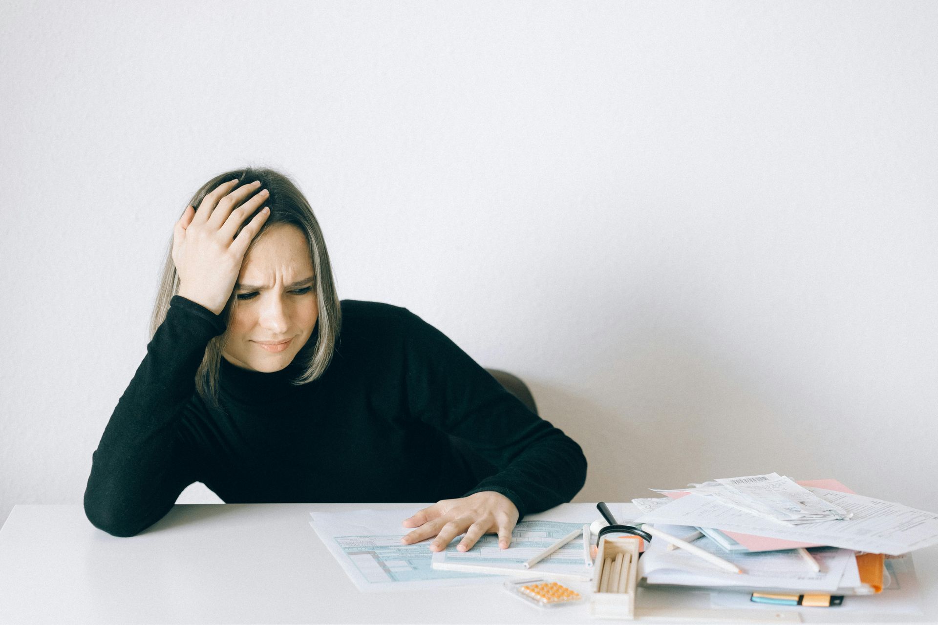 Woman with hand on head looking distressed at paperwork on a white desk.