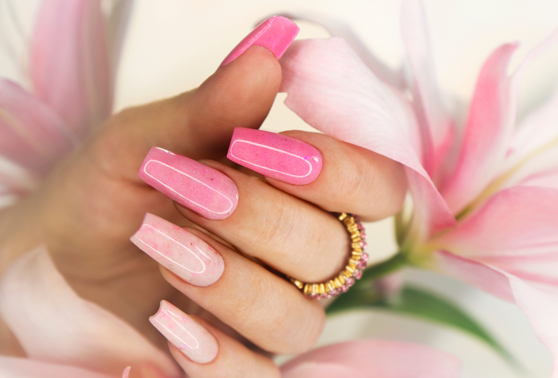 a woman 's hand with pink nails is holding a pink flower .