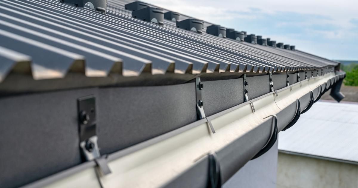 Close-up of a dark metal roof and gutter system on a building, showing details of the corrugated roof and gutter brackets.