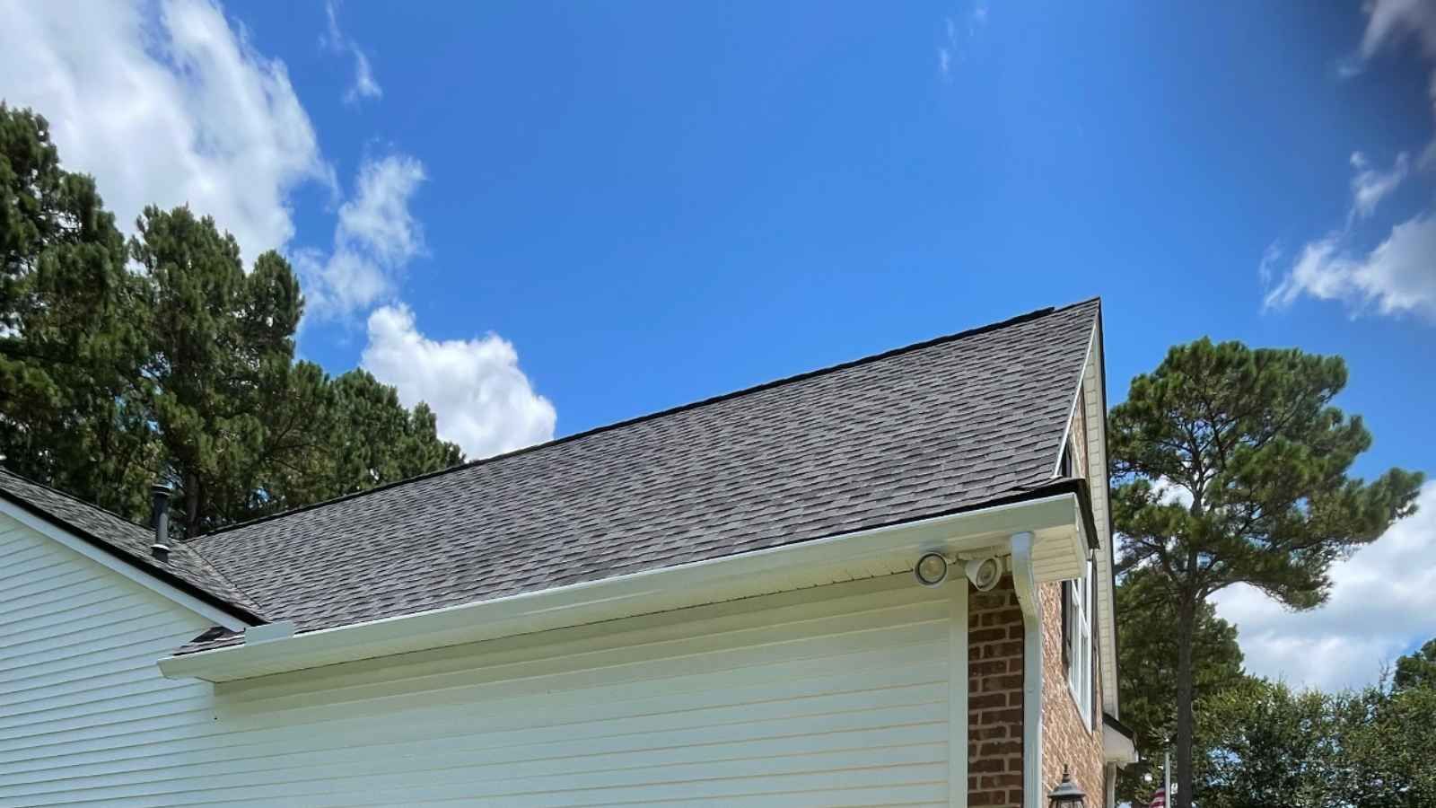 a white house with a gray roof with gutters and a blue sky in the background .