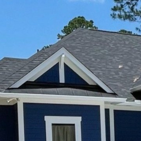 Blue house roof with gray shingles and a white-trimmed gable against a clear blue sky