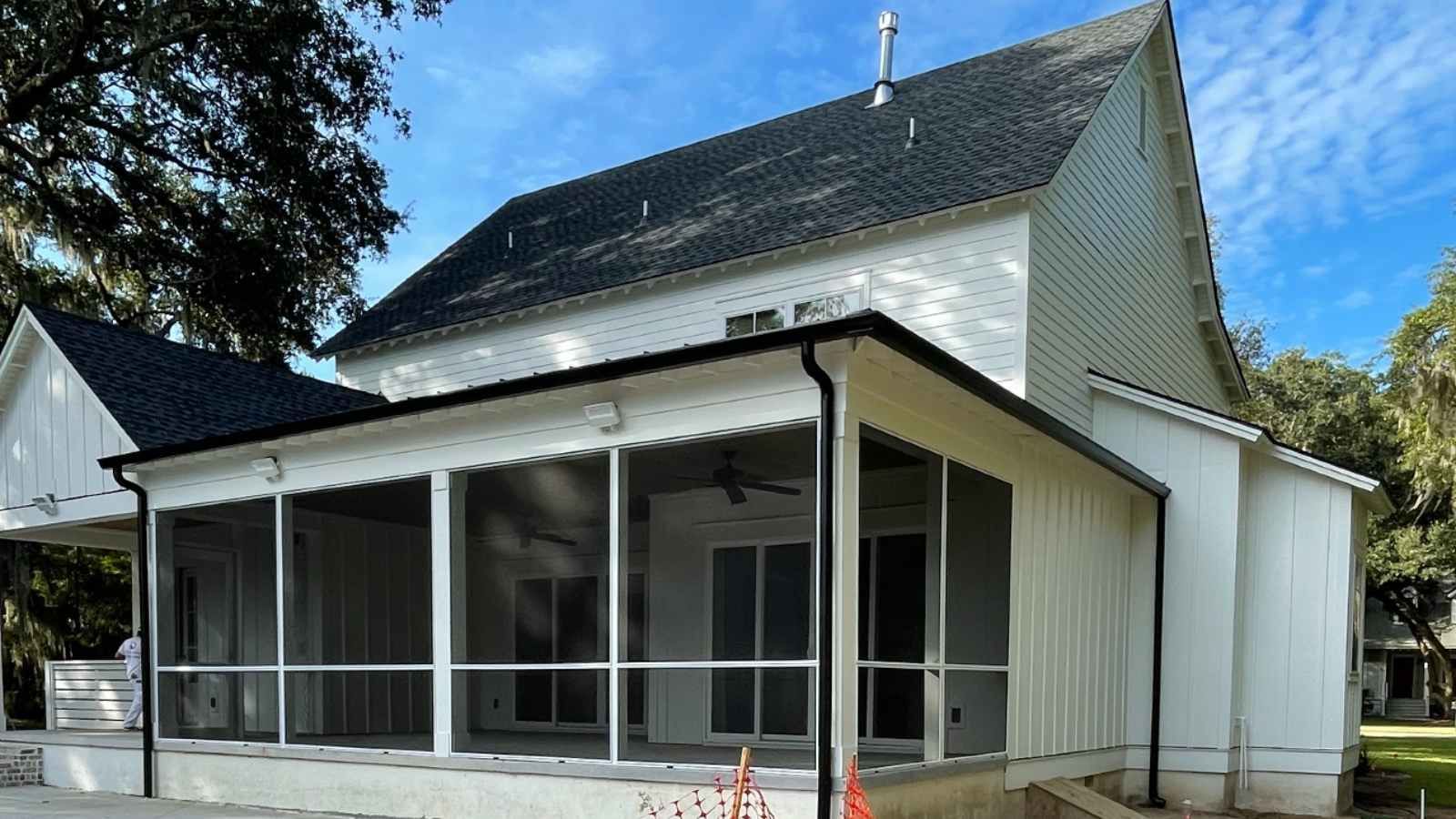 a white house with a screened in porch and a black roof with gutters .