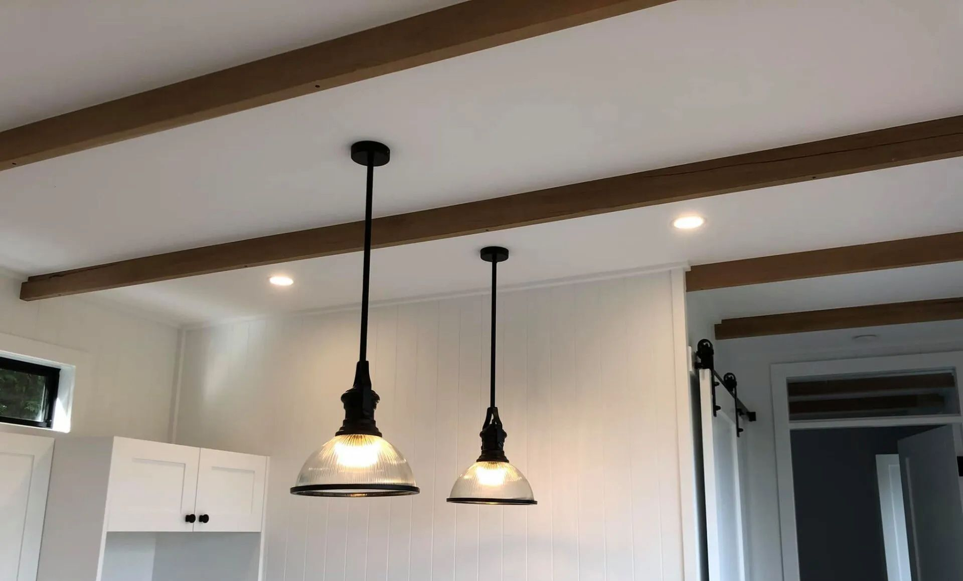 Kitchen with two black pendant lights hanging from a white ceiling with dark wood beams — Technik Electrical in Bowral, NSW