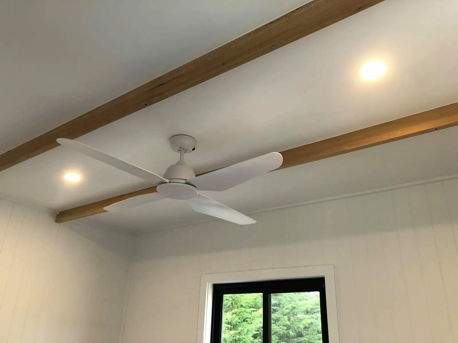 A White Ceiling Fan Mounted Between Two Light-wood Ceiling Beams in a Room — Technik Electrical in Renwick, NSW
