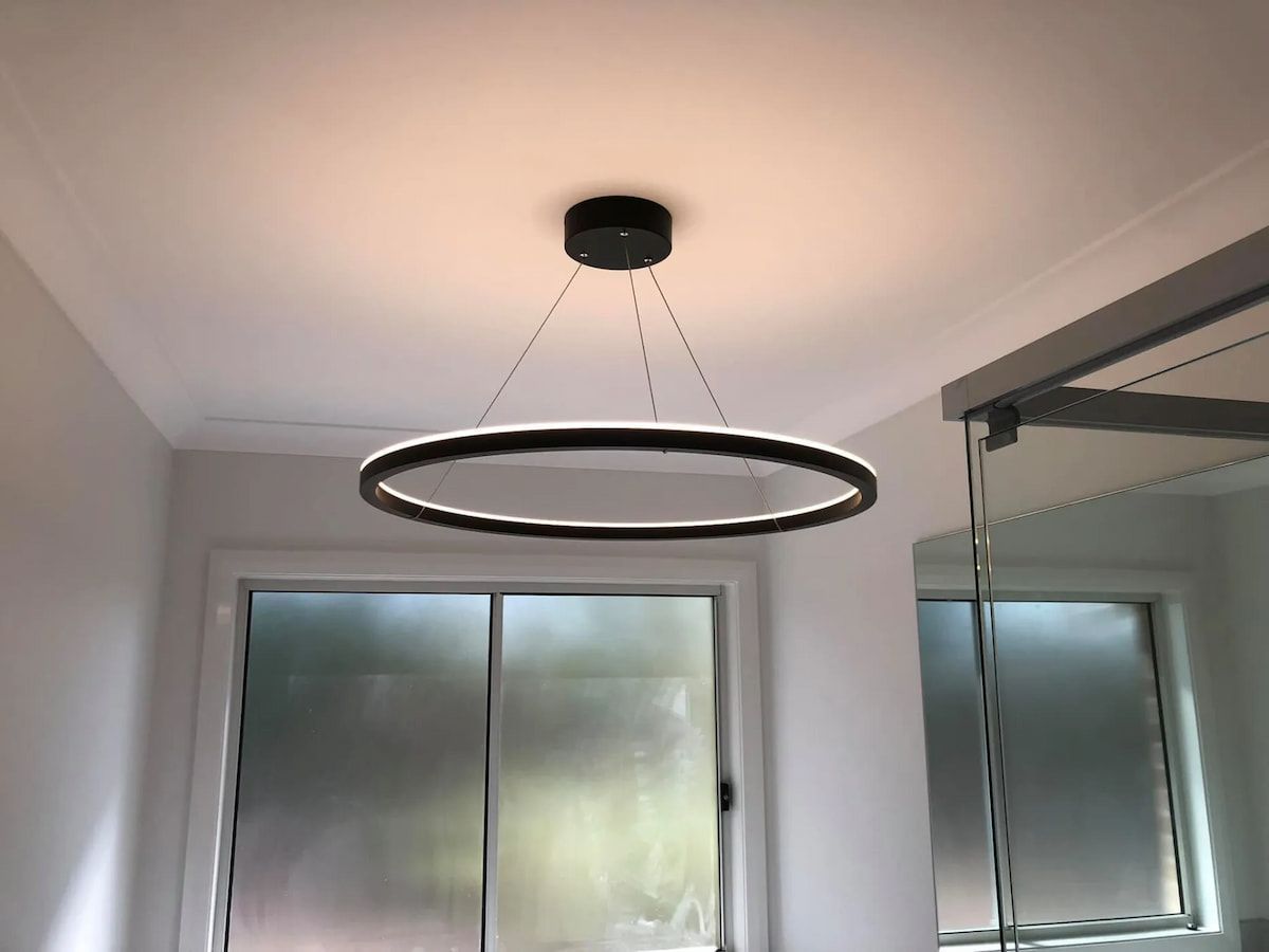 A Modern Black Circular Led Ring Pendant Light Hangs From a Ceiling in Front of a Window — Technik Electrical in Renwick, NSW