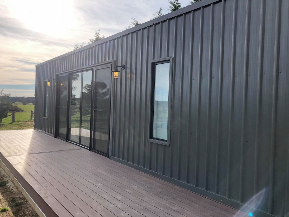 Dark gray modern building with large windows and a wooden deck at sunset — Technik Electrical in Bundanoon, NSW