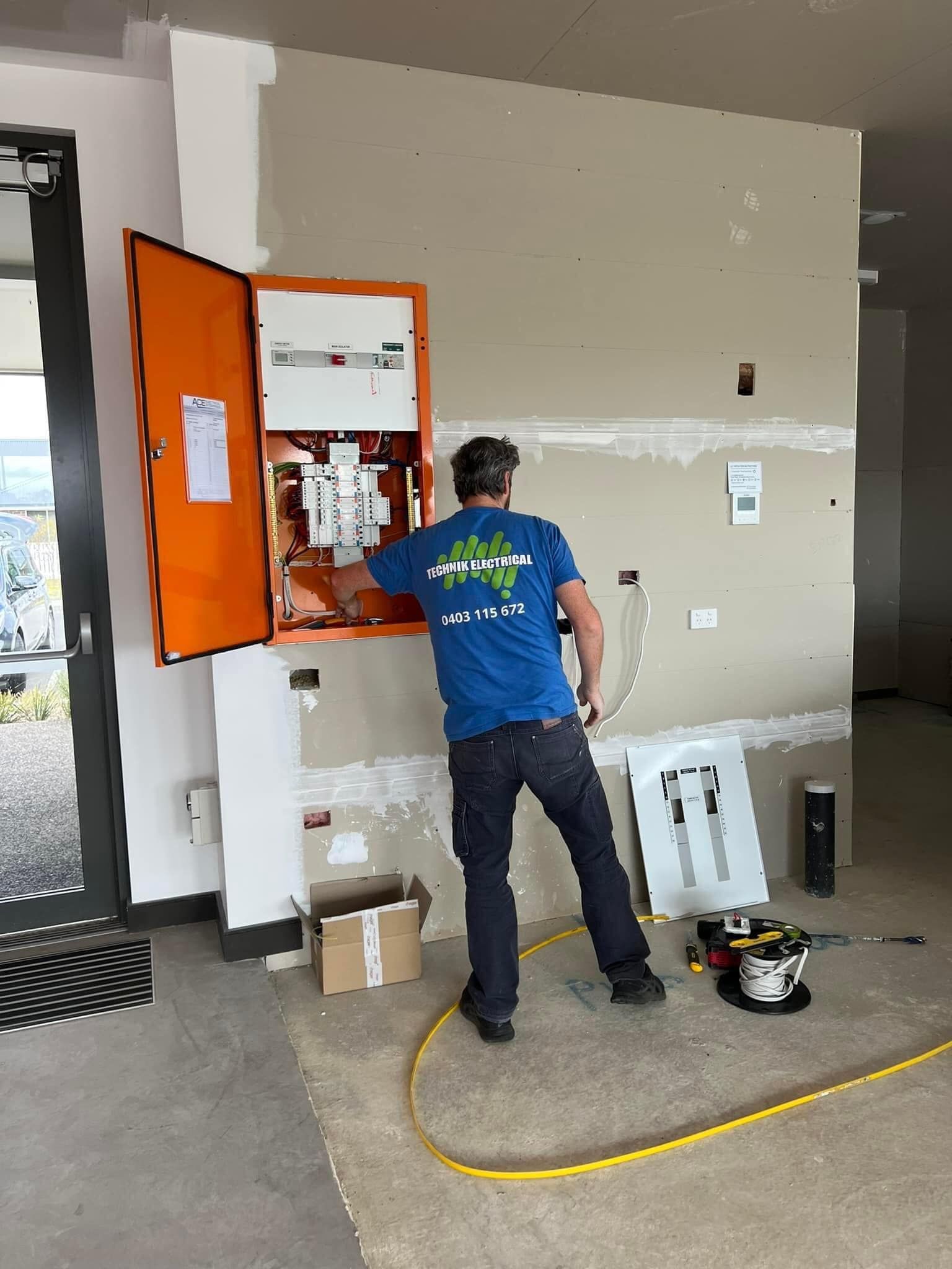 Person standing at an open orange cabinet in a utility room with tools on the floor. — Technik Electrical in Bundanoon, NSW