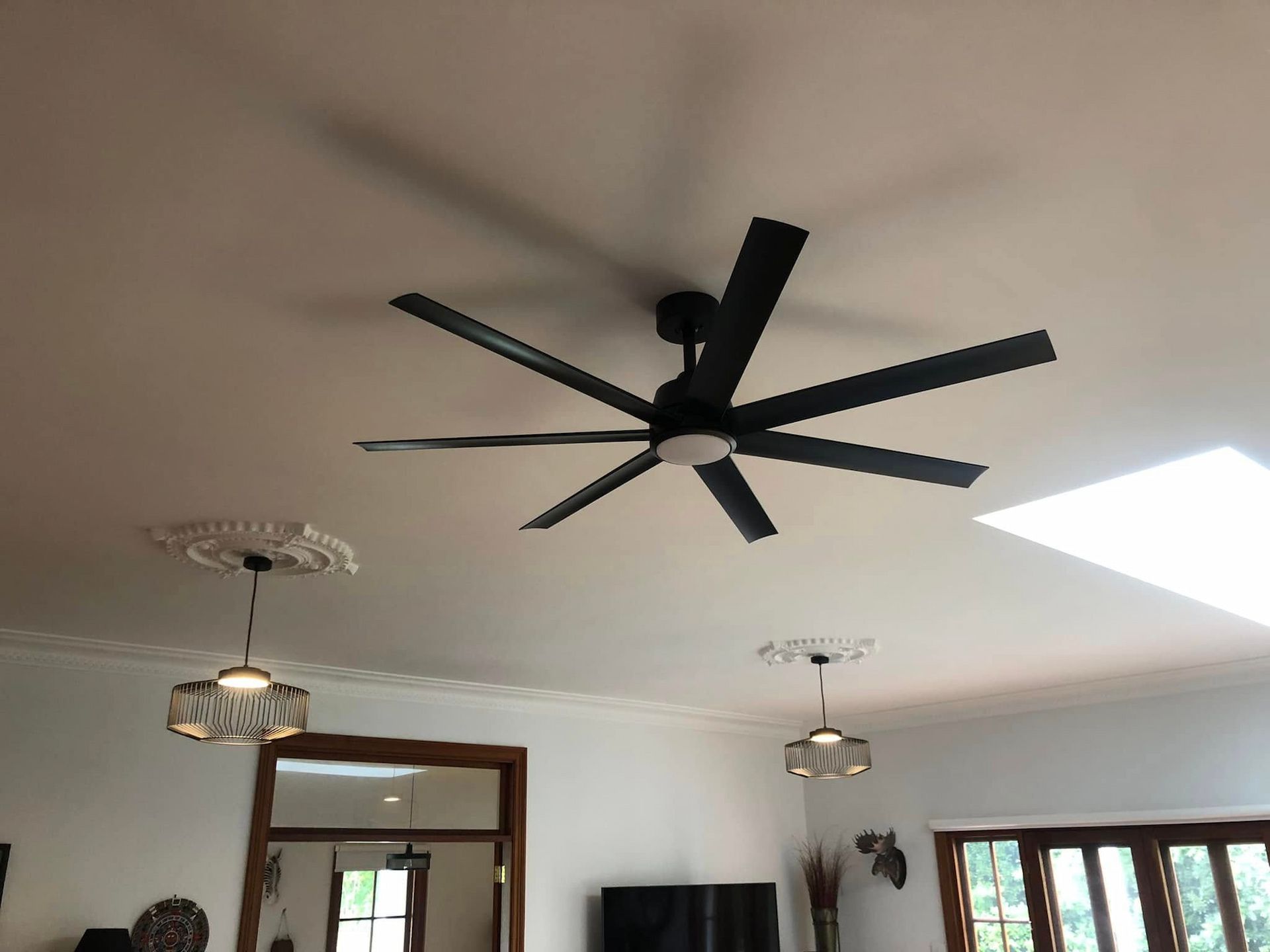 Living room ceiling with large black fan, white ceiling, windows, and hanging pendant lights — Technik Electrical in Mittagong, NSW
