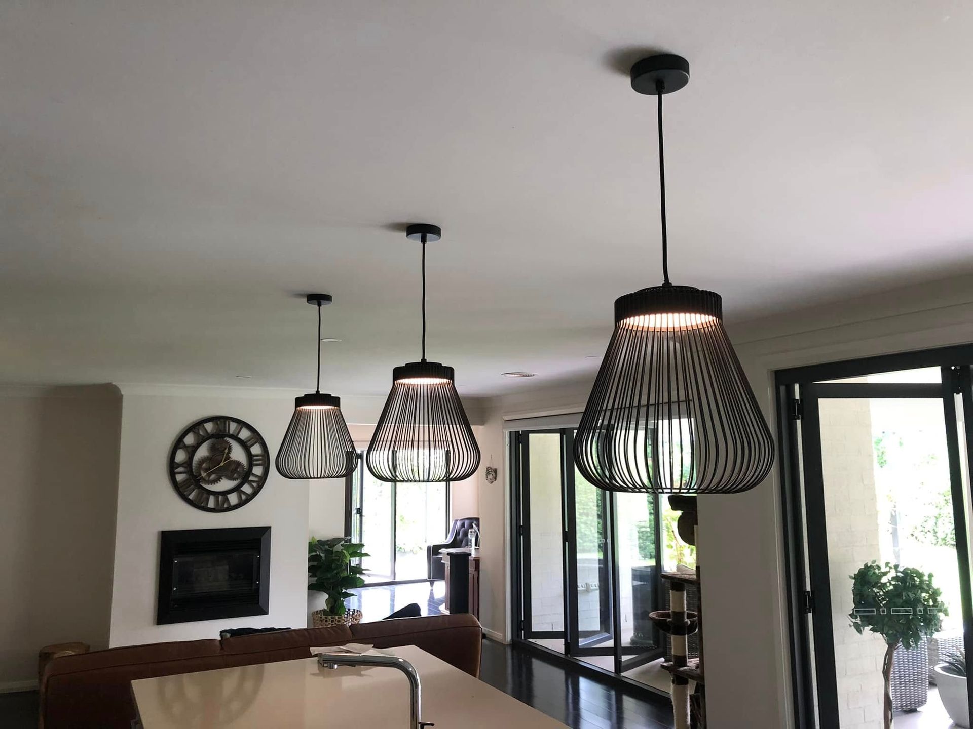 Modern living room with hanging pendant lights, wall clock, and bright patio doors — Technik Electrical in Bowral, NSW