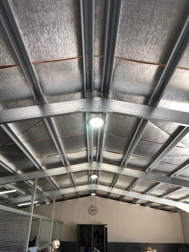 Interior ceiling of a metal-roofed structure with exposed beams and a bright hanging light — Technik Electrical in Renwick, NSW