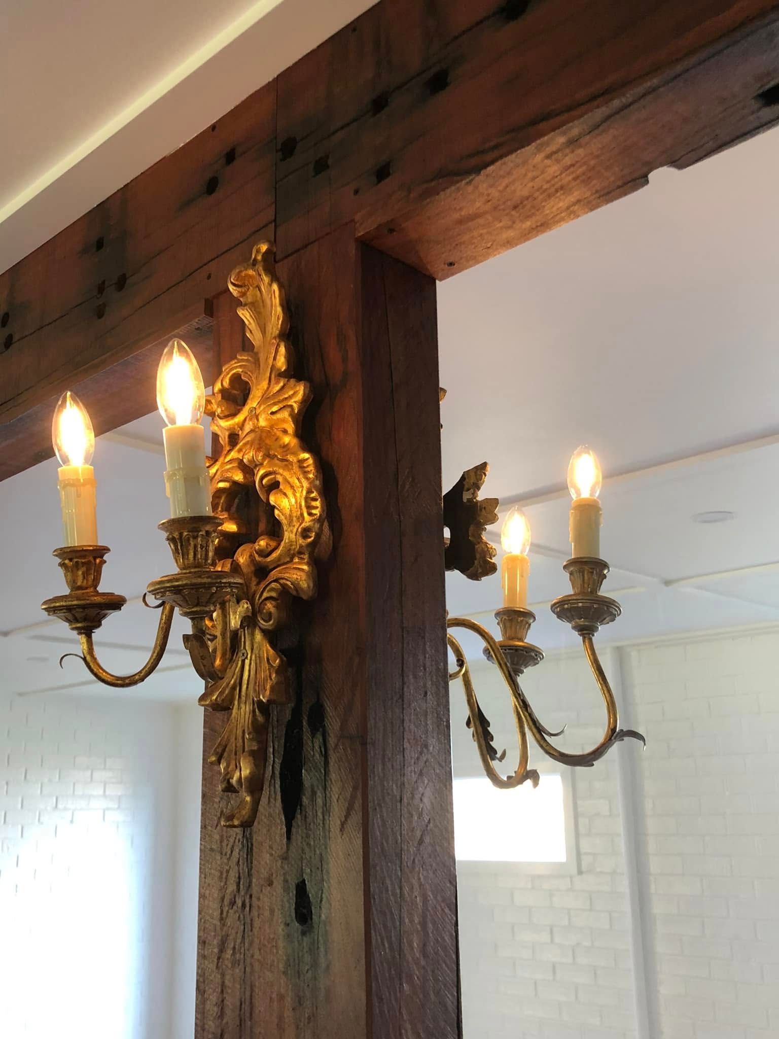 Ornate gold wall sconce with lit candles mounted on a dark wooden beam in a bright room — Technik Electrical in Bowral, NSW