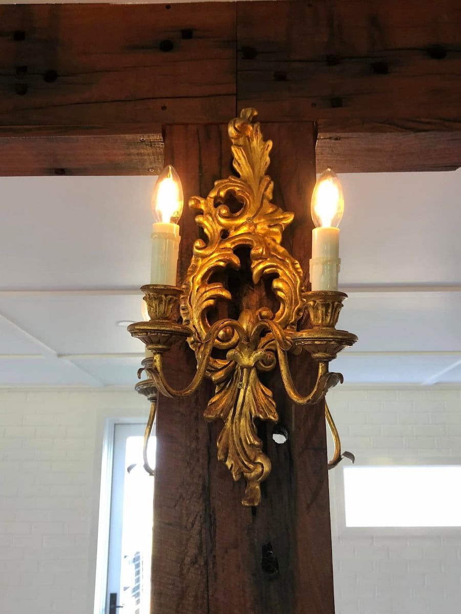 Ornate gold wall sconce with two lit candles mounted on a wooden beam — Technik Electrical in Bundanoon, NSW