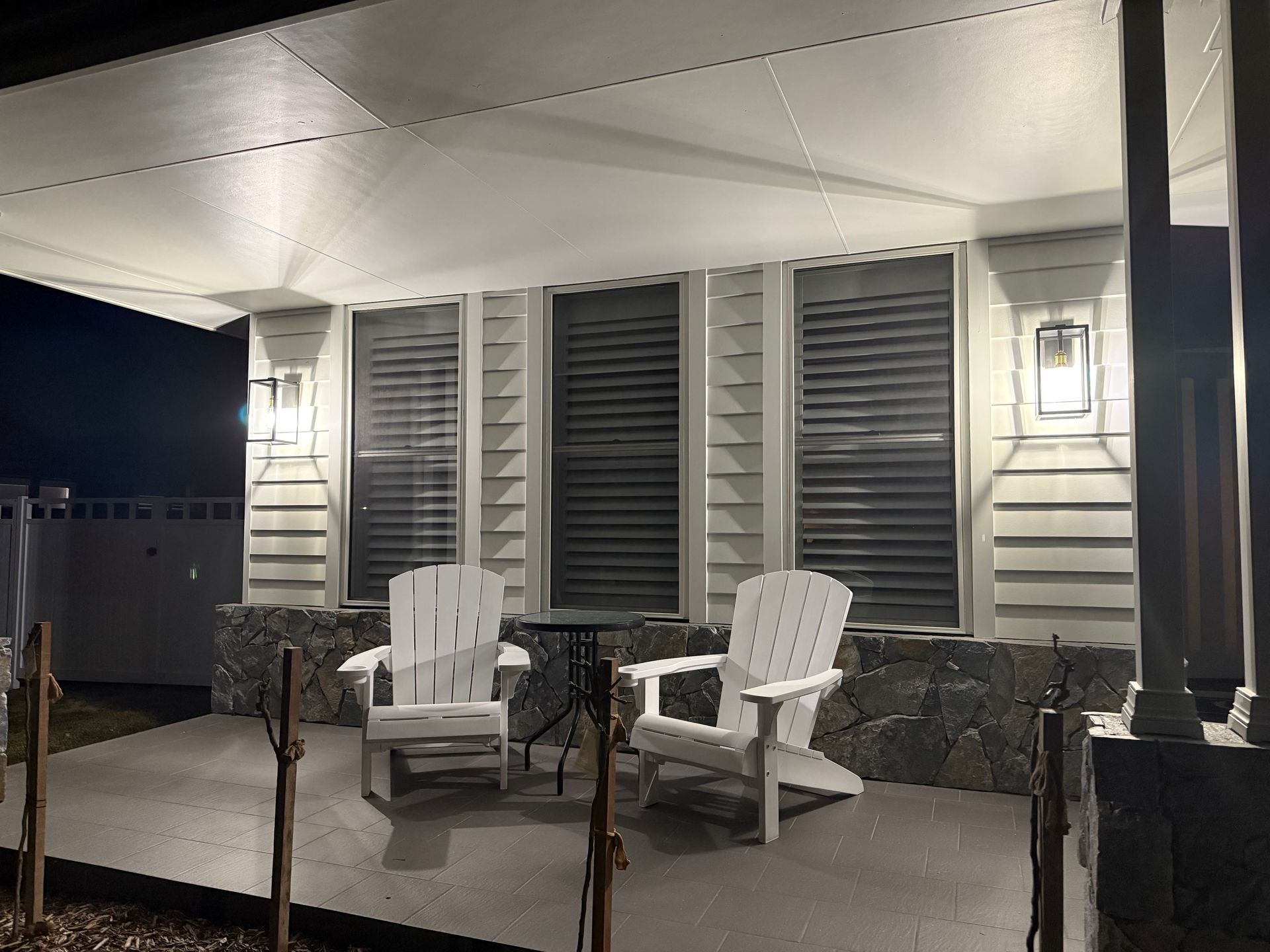 Covered porch with two white chairs, small tables, and lit wall lanterns at night — Technik Electrical in Renwick, NSW
