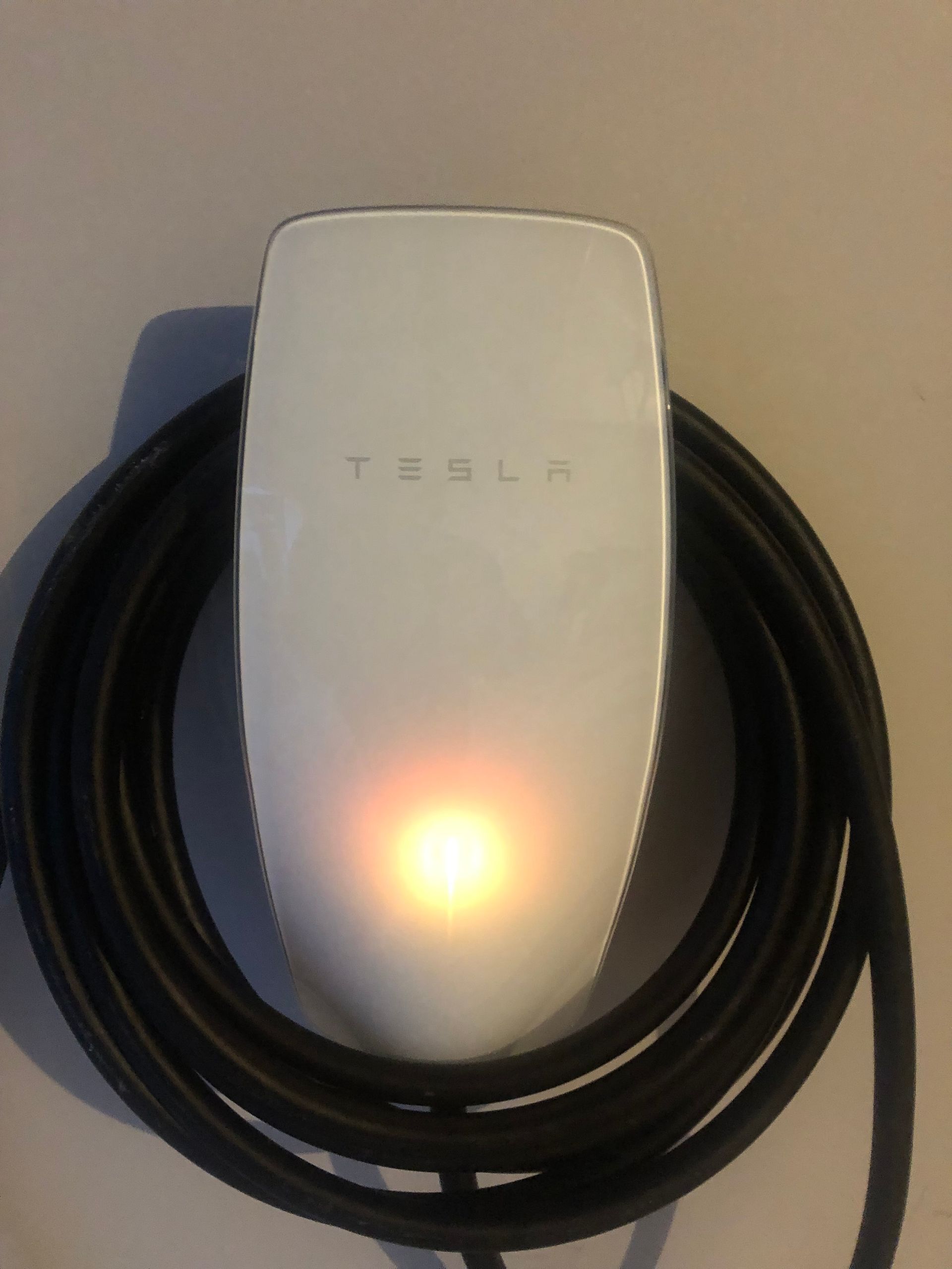 White Tesla device with a glowing amber light, wrapped in a coiled black cable on a wall or shelf. — Technik Electrical in Mittagong, NSW