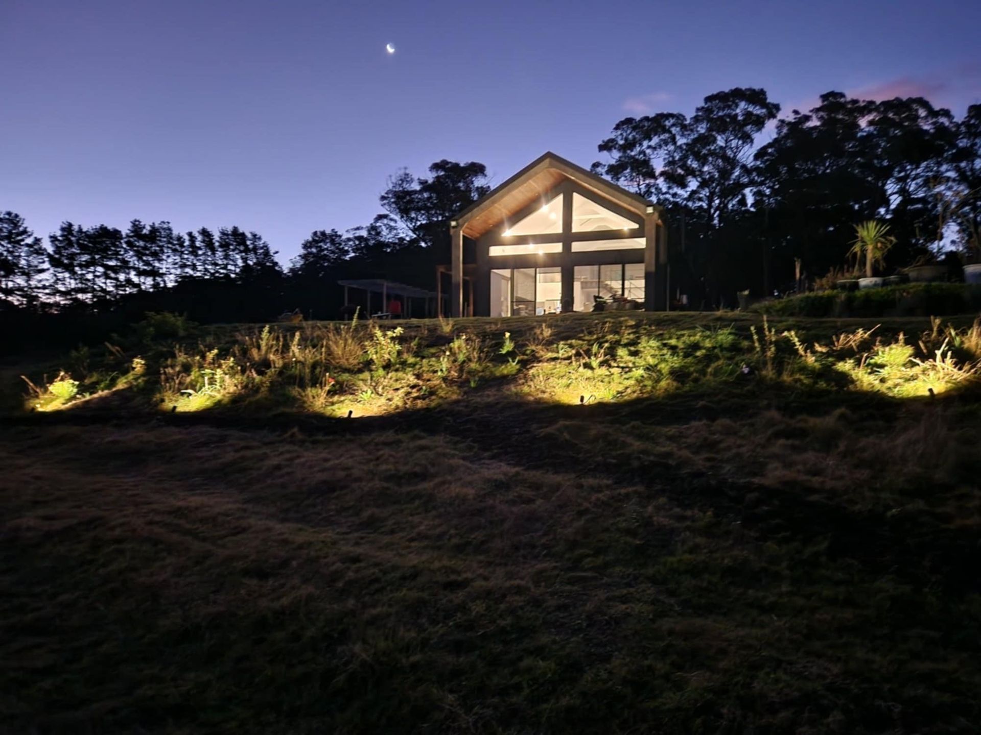 Lit house at dusk on a hillside, with illuminated garden lights and a moonlit sky. — Technik Electrical in Renwick, NSW