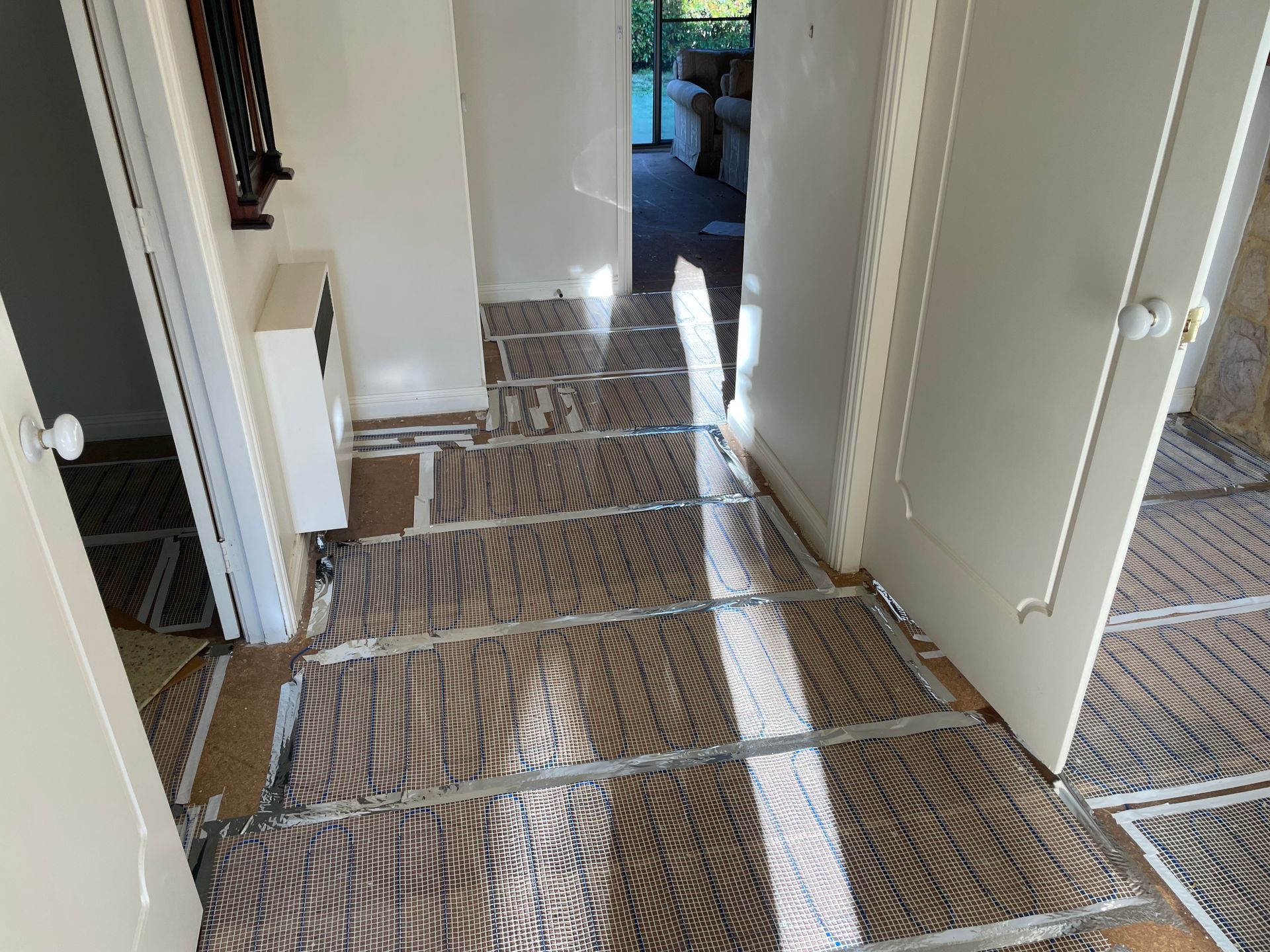Hallway with plastic-covered floors and open doors, lit by sunlight from a back room — Technik Electrical in Renwick, NSW