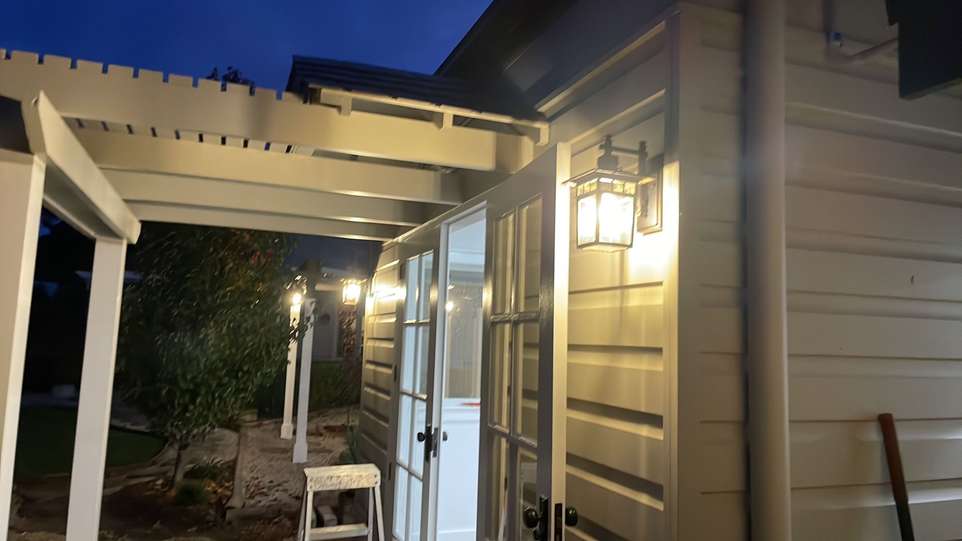 Nighttime view of a house exterior with lit porch lights, beige siding, and a covered patio walkway — Technik Electrical in Renwick, NSW