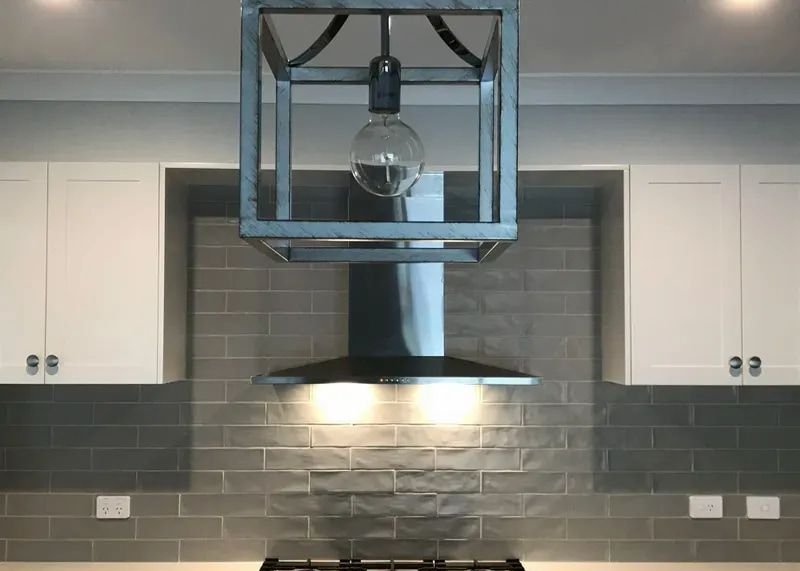 A Modern Kitchen Stove With a Stainless Steel Range Hood, Grey Subway Tile Backsplash — Technik Electrical in Renwick, NSW