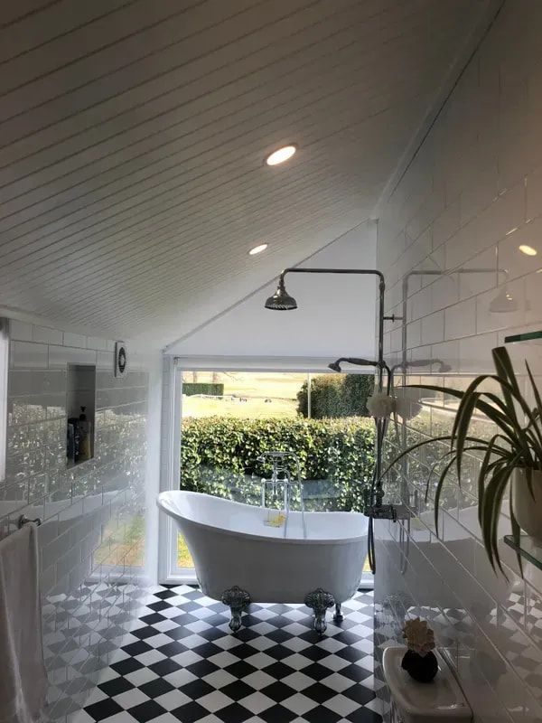 Modern bathroom with a freestanding tub, black-and-white floor tiles, and a shower by a large window. — Technik Electrical in Bundanoon, NSW