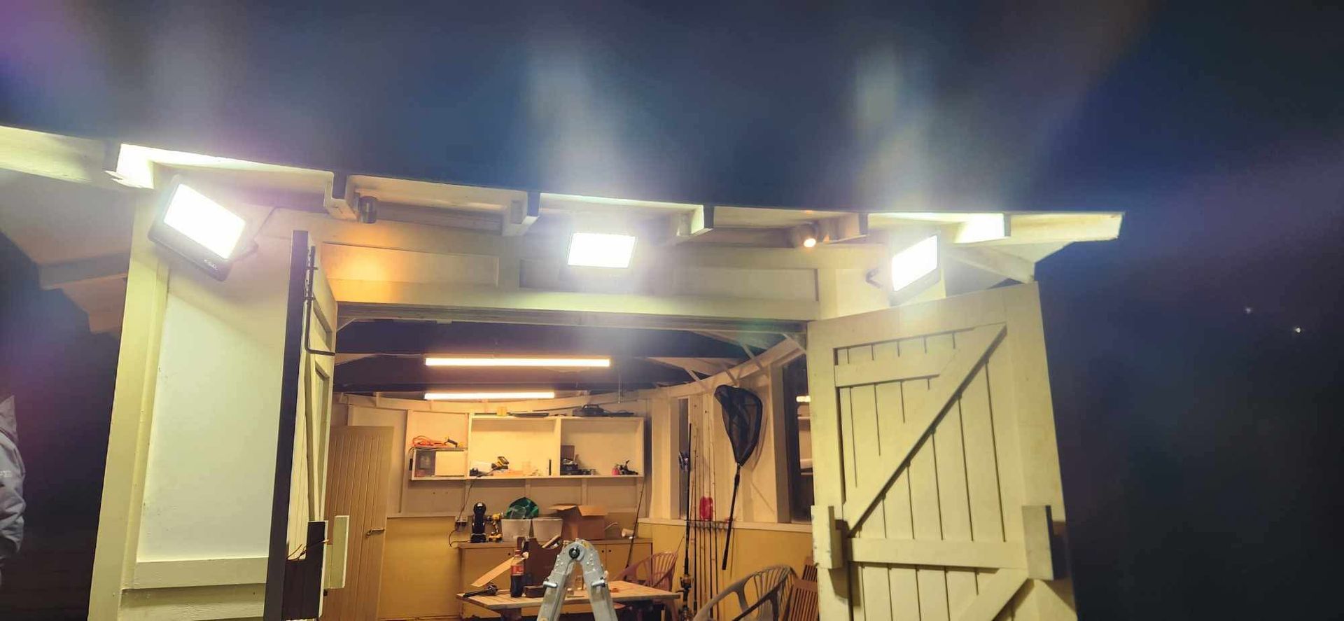 Open wooden cabin entrance lit at night, with shelves and a seated person inside. — Technik Electrical in Renwick, NSW