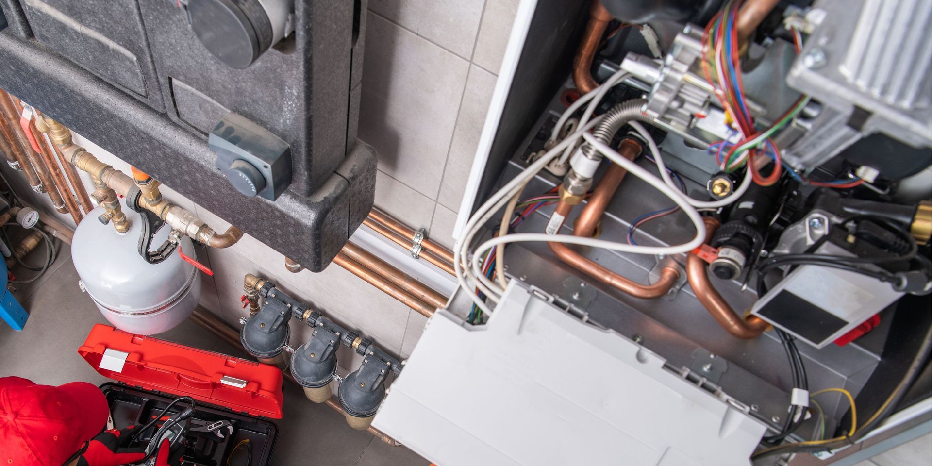 Close-up of a heating system installation with copper pipes, wiring, and a toolbox.