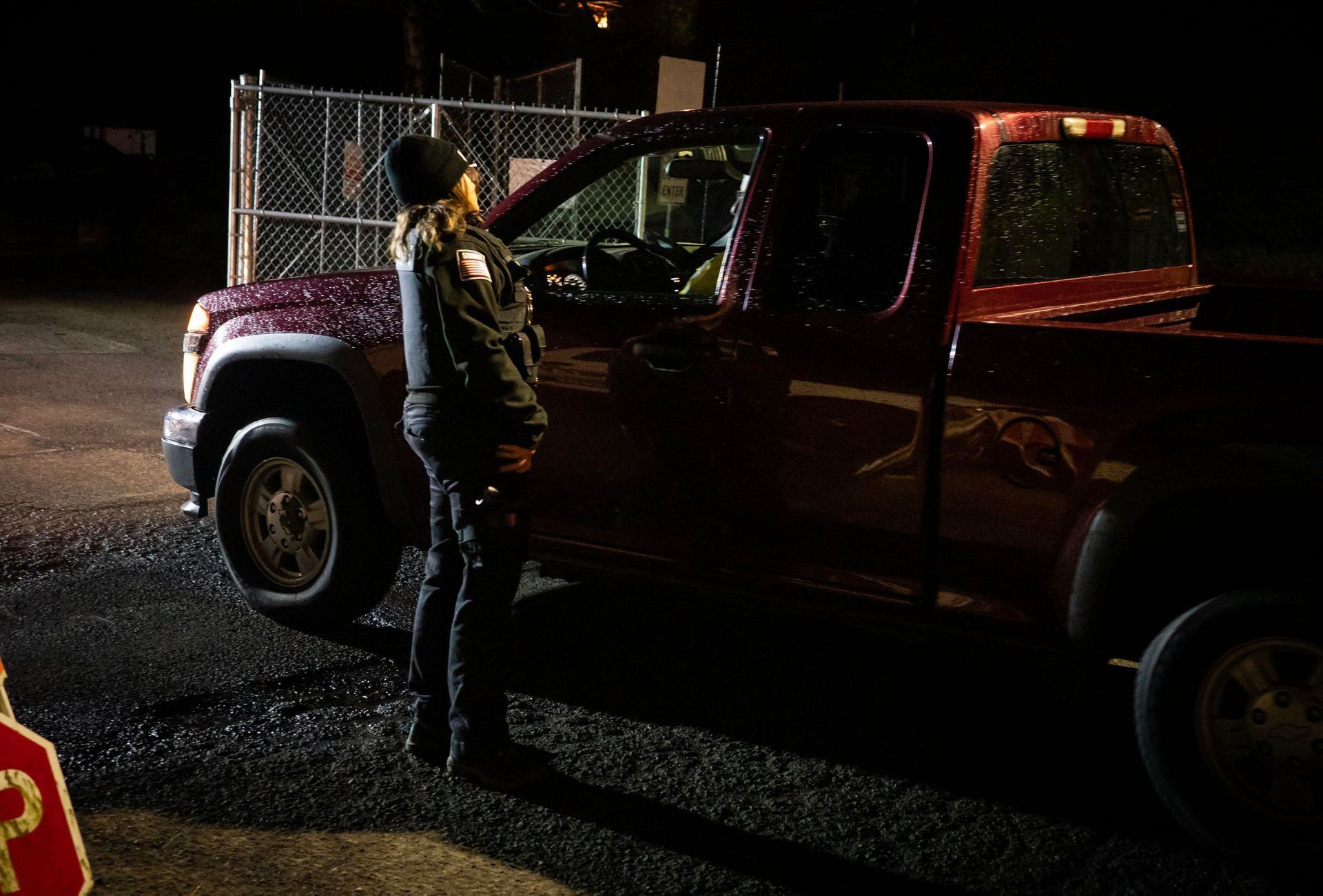 Person standing beside a maroon pickup truck at night on a wet street