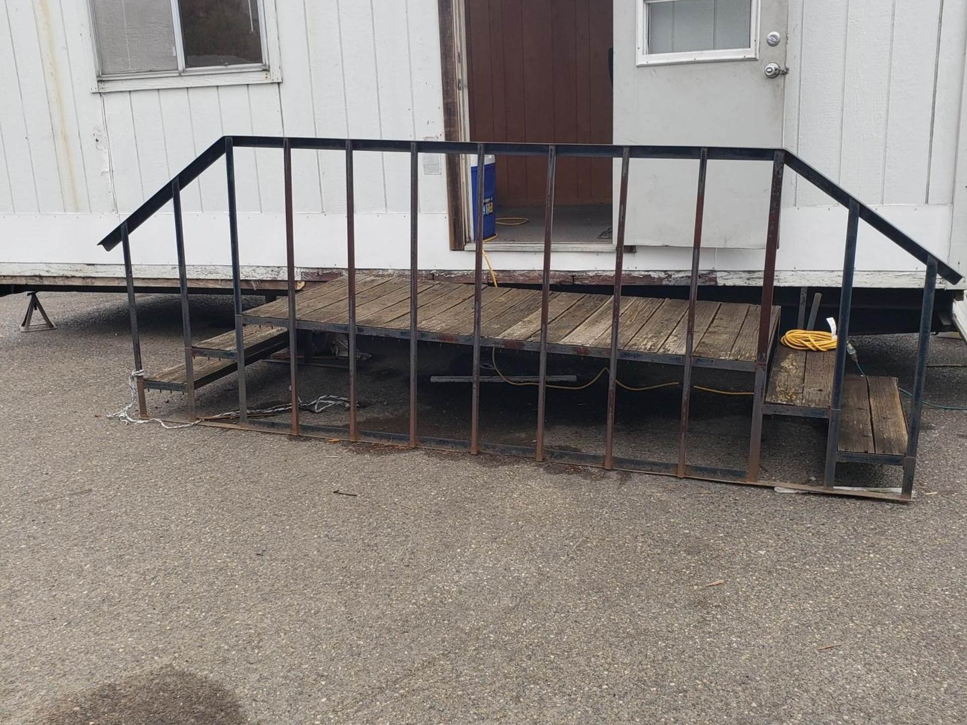 Black metal ramp with railings leading to a house entrance on a gravel driveway.