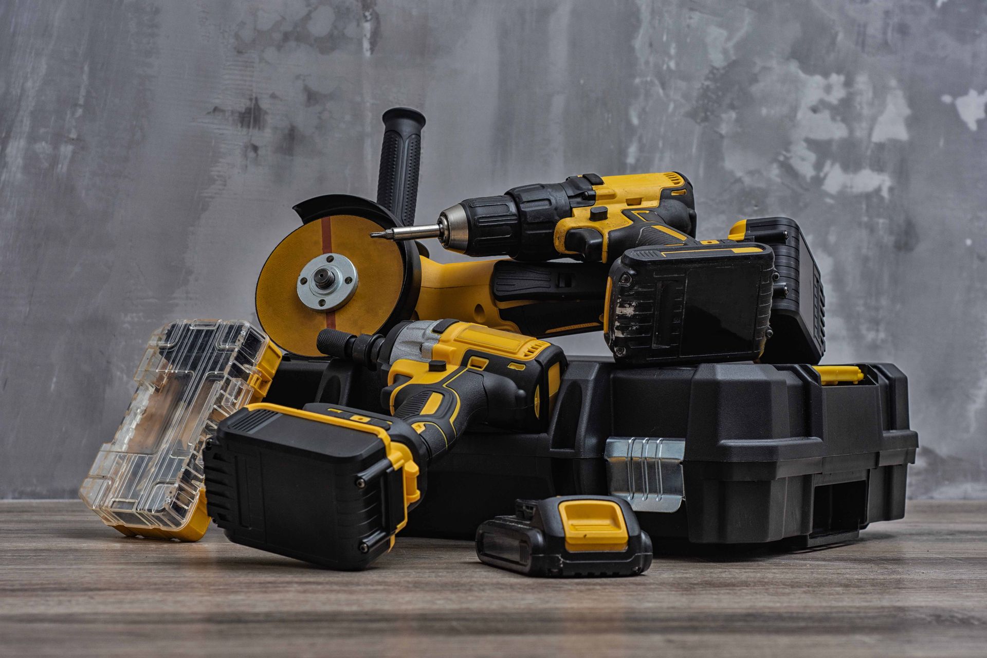 Black-and-yellow cordless power tools and accessories arranged on a wooden surface against a gray wall